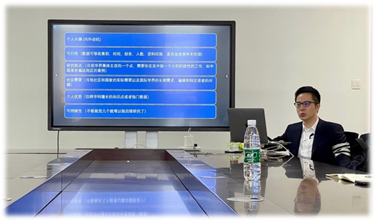 A person sitting at a desk with a computer and a large screen Description automatically generated with low confidence